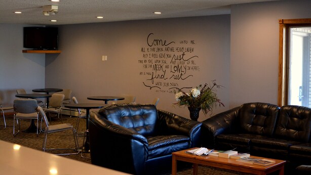 A lounge area with leather seating, a flat-screen TV mounted on the wall, and a wall with inspirational text. - Dutch Country Inn (Kalona)