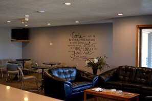 A lounge area with leather seating, a flat-screen TV mounted on the wall, and a wall with inspirational text. - Dutch Country Inn (Kalona)