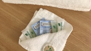 A white towel with a black cloth labeled "Makeup Remover" and a white cloth containing several green and blue facial care products. - Dutch Country Inn (Kalona)