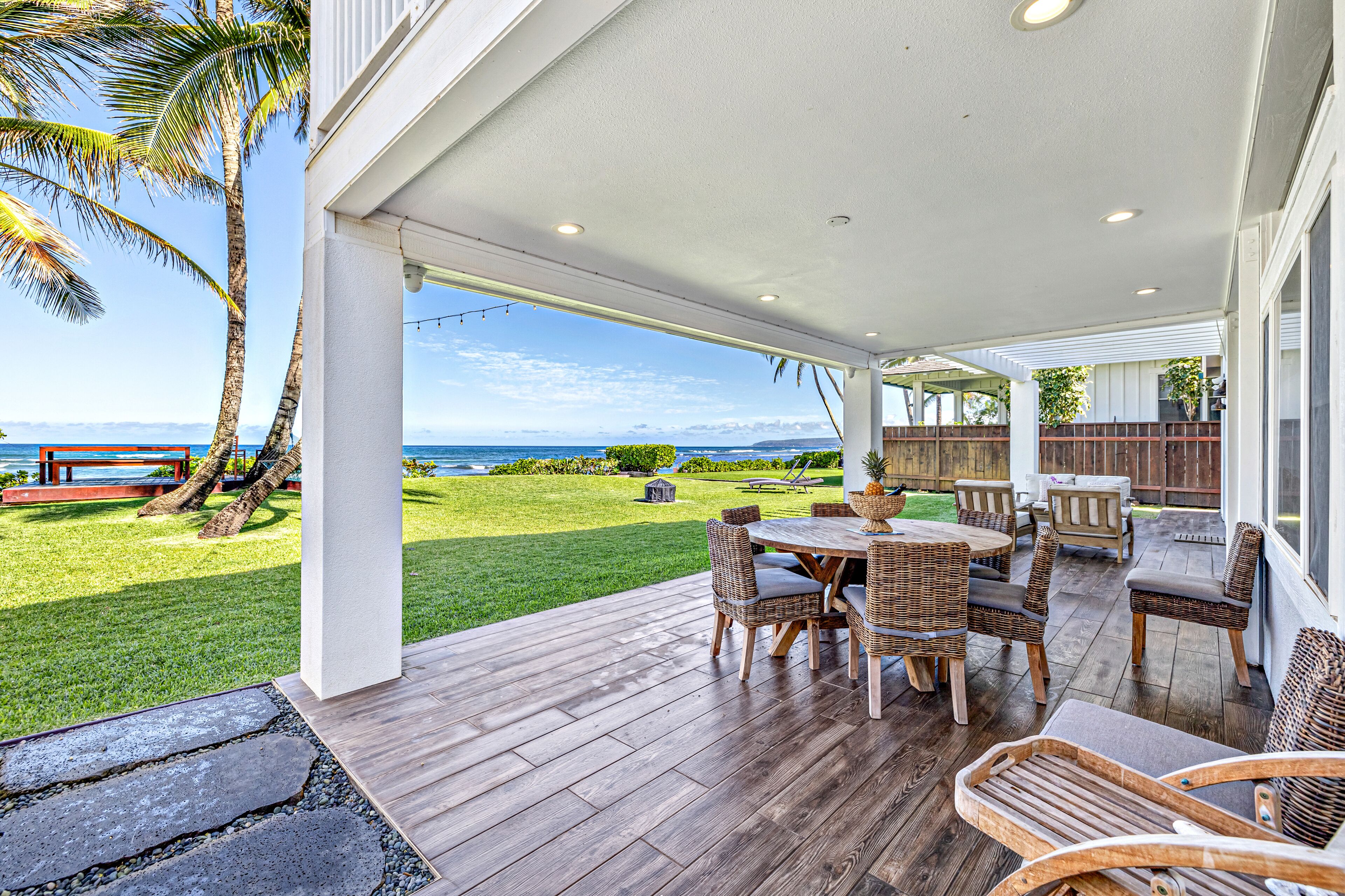 A covered patio with a wooden deck, wicker furniture, and a view of the ocean.
