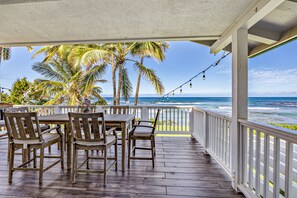 A wooden deck with a table and chairs, overlooking a beach with palm trees and the ocean. - Oceanfront Family Escape w/ A/C, Large Yard and Sunset Deck (Waialua)