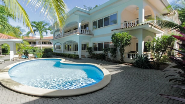 A large, circular swimming pool surrounded by a paved area with a multi-story building featuring balconies and large windows. - Ocean Breeze 11 (Sardinal)