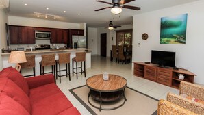A modern living room with a red sofa, a round wooden coffee table, and wicker chairs. - Ocean Breeze 11 (Sardinal)