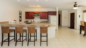 A modern kitchen with a central island, bar stools, a microwave, and a refrigerator. - Ocean Breeze 11 (Sardinal)