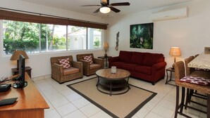 A living room with a red sofa, wicker chairs, a coffee table, and a TV on a wooden desk. - Ocean Breeze 11 (Sardinal)