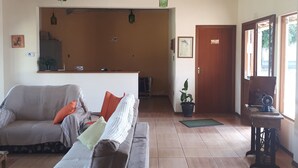Una sala de estar con un sofá, una mesa de centro y una máquina de coser. Hay una puerta que da a otra habitación y una ventana con vistas al exterior.