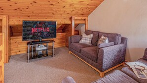 Ein gemütliches Holzhaus mit einem Fernseher, auf dem das Netflix-Logo zu sehen ist, einem braunen Sofa und einem kleinen Tisch mit einer Fernbedienung.