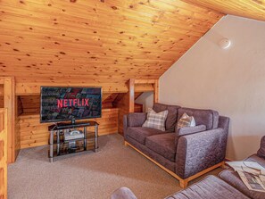 Ein gemütliches Holzhaus mit einem Fernseher, auf dem das Netflix-Logo zu sehen ist, einem braunen Sofa und einem kleinen Tisch mit einer Fernbedienung.