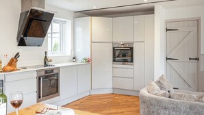Eine moderne Küche mit weißen Schränken, einem eingebauten Ofen und einem Essbereich mit einem Holztisch und einem grauen Sofa.
