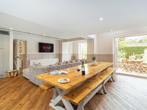 Uma sala de estar moderna com uma mesa de jantar de madeira, um sofá e uma televisão fixada na parede.