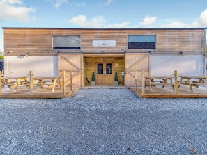 A wooden barn-style building with a gravel driveway and picnic tables.