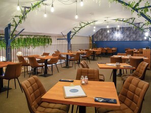 A restaurant with multiple tables and chairs, a blue wall, and hanging plants.