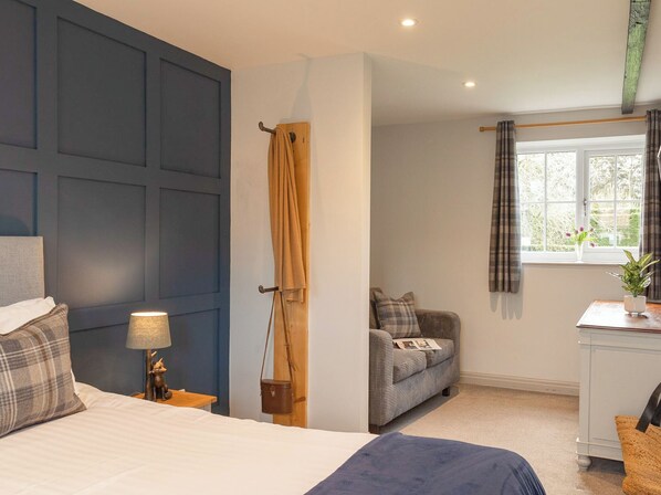 A bedroom with a bed, bedside table, lamp, and a view of a living area with a sofa and window.