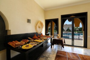 A buffet table with various dishes, a decorative wall piece, and a view of an outdoor pool area through a glass door. - Atlas Widan (Marrakech)