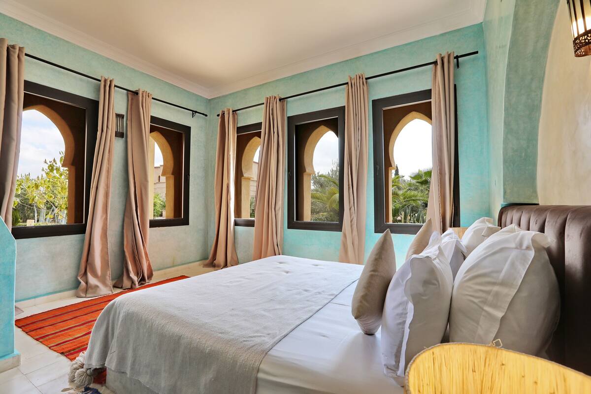 Quarto com cama, cortinas e janelas em arco.