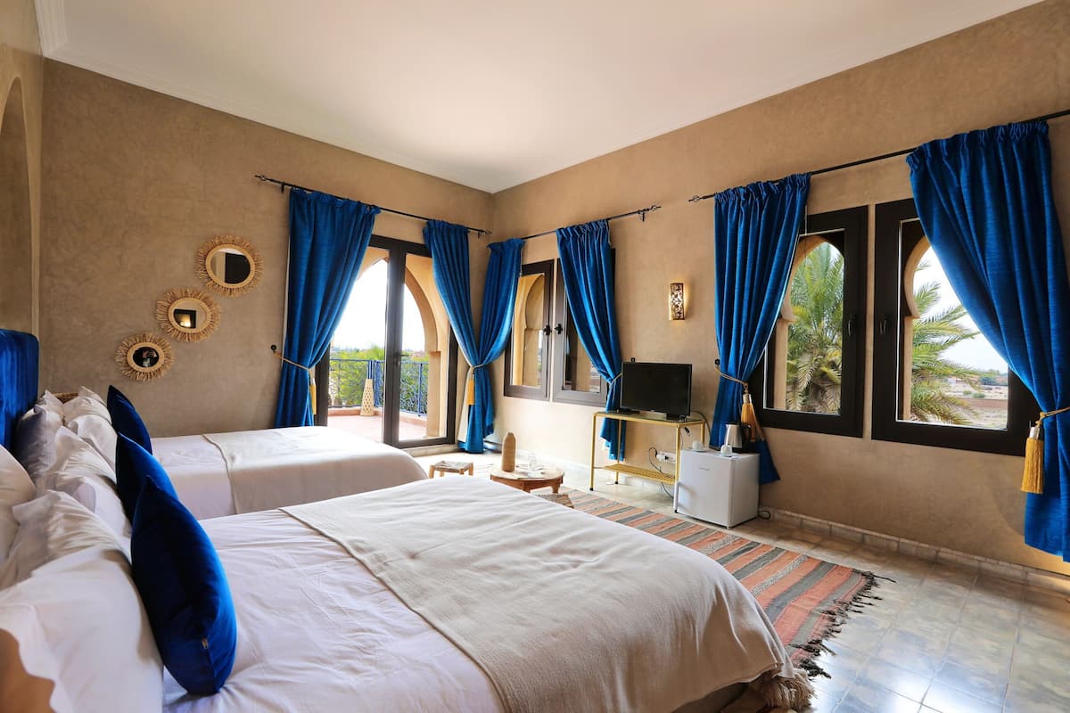 Quarto de hotel com duas camas, televisão, uma mesinha e uma janela com cortinas azuis.