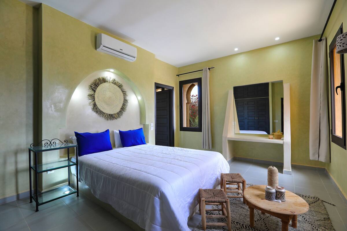 Quarto com cama, mesa de cabeceira, espelho e janela com cortinas.