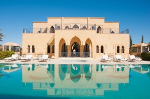 Ein Hotel mit einem großen Pool, mehreren Bögen und einem Balkon mit Liegestühlen.