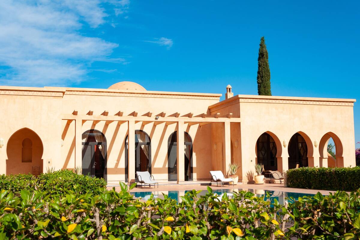 Um edifício com piscina, janelas em arco e céu claro.