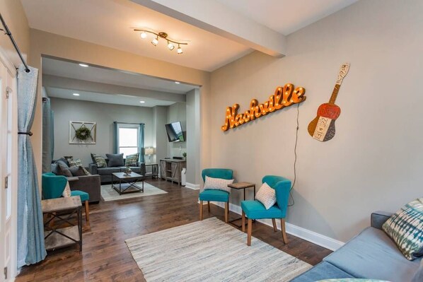Una sala de estar moderna con un sofá, sillas, una mesita de centro y un adorno de guitarra colgada en la pared.