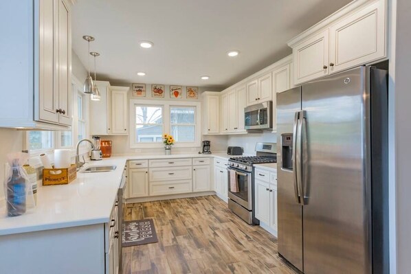 A modern kitchen with white cabinets, stainless steel appliances, and a wooden floor.