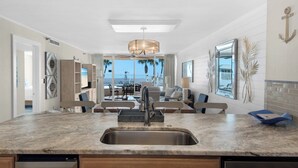 A modern kitchen with a central island, a built-in sink, and a dining area with a view of the ocean. - Private Poolside Patio, Beachfront Condo, Free Beach Service (Miramar Beach)