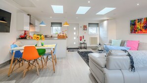 A modern living room with a sofa, a dining area with a table and chairs, and a kitchen with a window. - 2 bedroom accommodation in Caldercruix, near Airdrie (Caldercruix, near Airdrie)