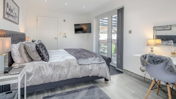A modern bedroom with a bed, bedside table, lamp, and a television on the wall. - 2 bedroom accommodation in Caldercruix, near Airdrie (Caldercruix, near Airdrie)