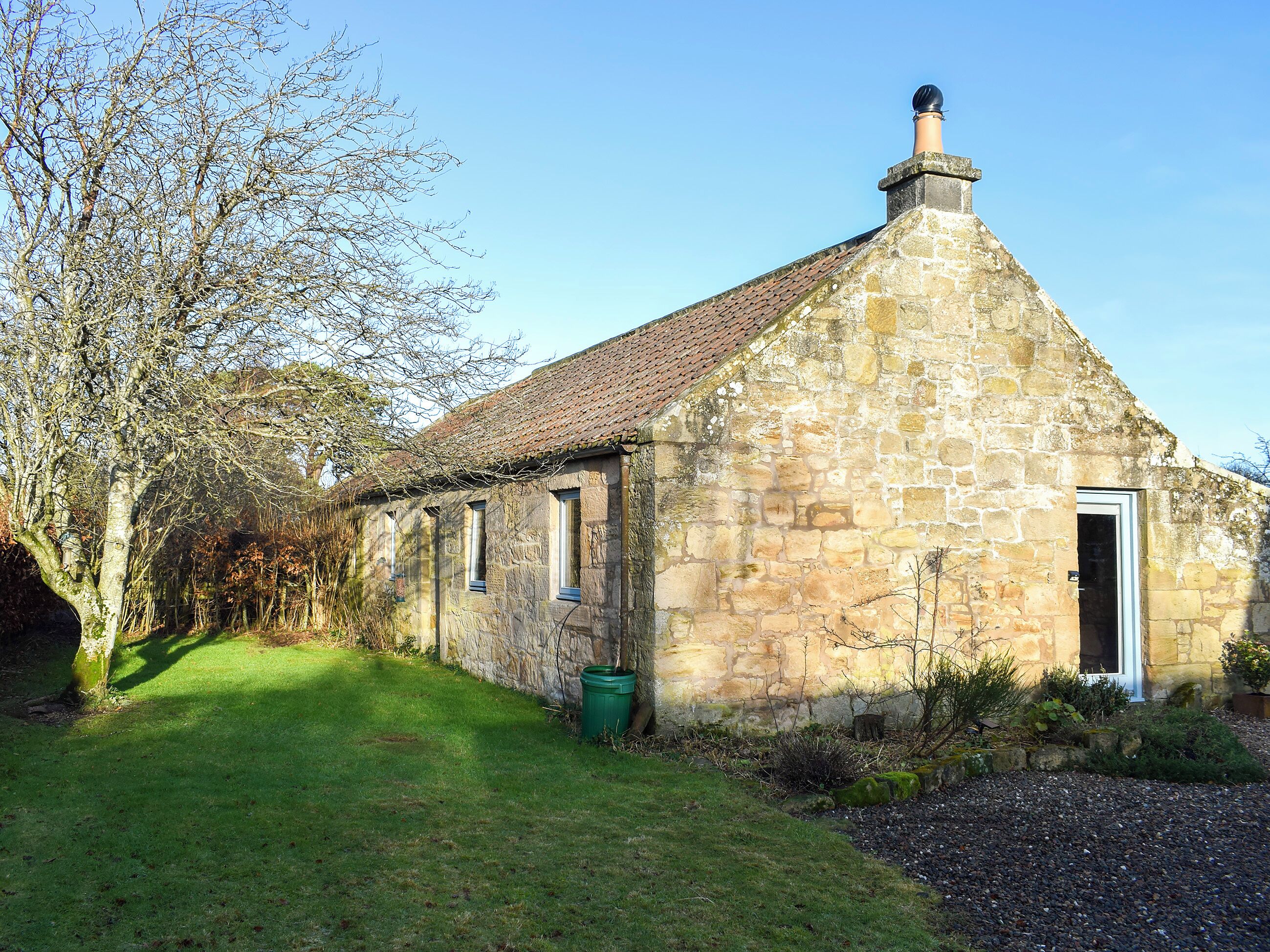 A stone building with a sloped roof, a chimney, and a door.