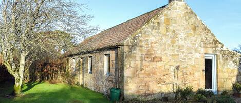 A stone building with a sloped roof, a chimney, and a door.