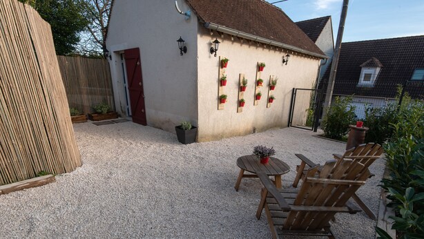A gravel patio with wooden chairs and a table, a white building with a red door, and potted plants on the wall. - J&J Room - Exceptional accommodation near Provins. www.jj-accommodation.fr (Saint-Loup-de-Naud)