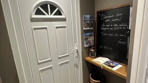 A hallway with a white door, a chalkboard with handwritten text, and a small shelf with books and a lantern. - J&J Room - Exceptional accommodation near Provins. www.jj-accommodation.fr (Saint-Loup-de-Naud)