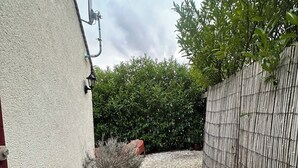 A gravel pathway leading to a white wall with a satellite dish, a red door, and a bamboo fence. - J&J Room - Exceptional accommodation near Provins. www.jj-accommodation.fr (Saint-Loup-de-Naud)