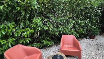 A seating area with two chairs and a small table, surrounded by gravel and a dense hedge.