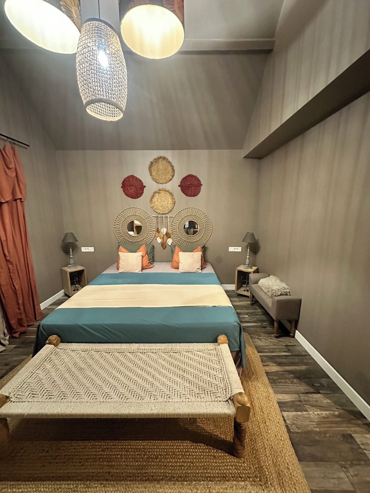 Een slaapkamer met een bed, twee nachtkastjes, een bankje, en een muur met decoratieve spiegels en kunst aan de muur.