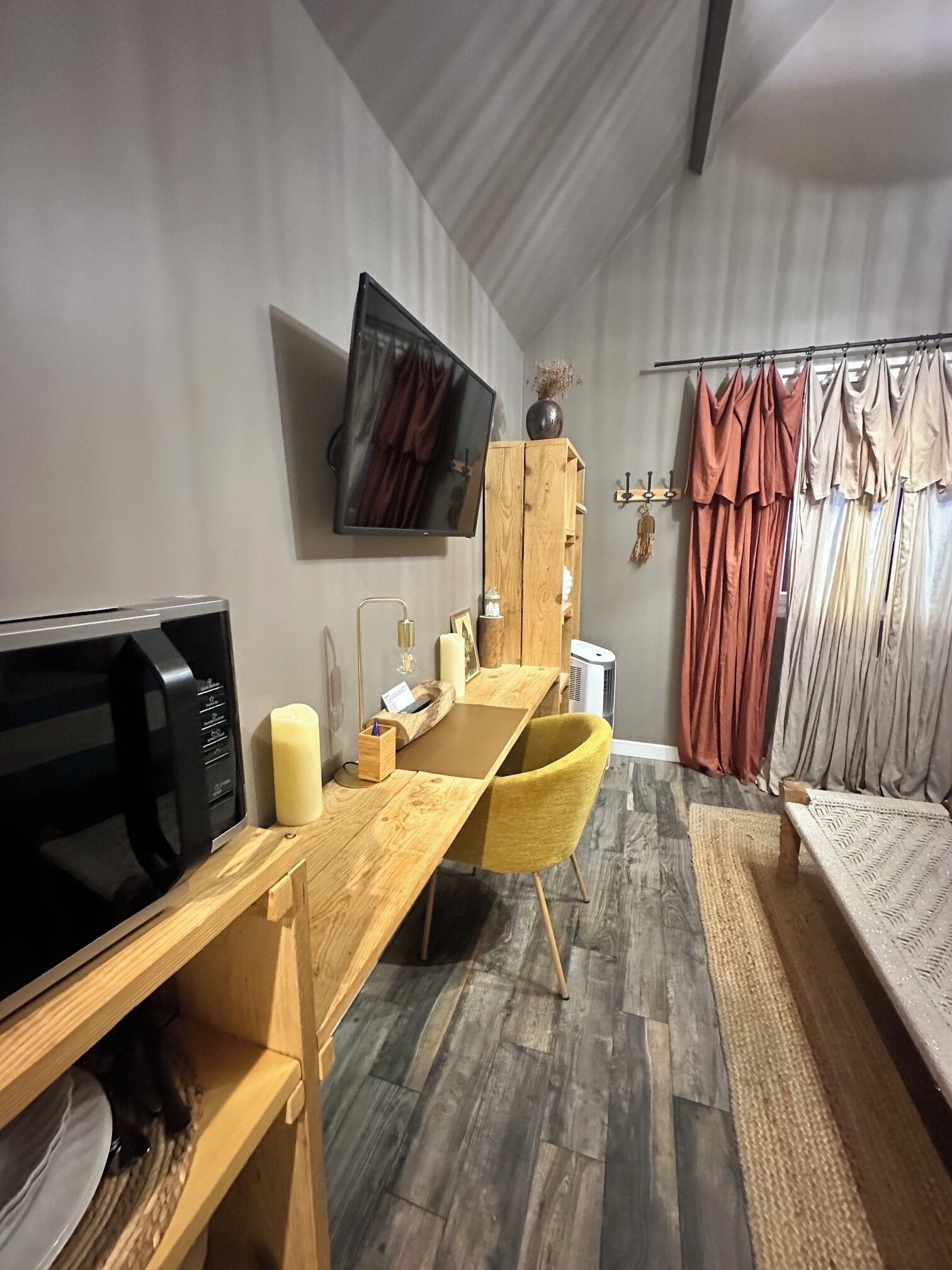 Een knus woongedeelte met een eethoek, een flatscreen televisie aan de muur, een houten kast en een raam met gordijnen.