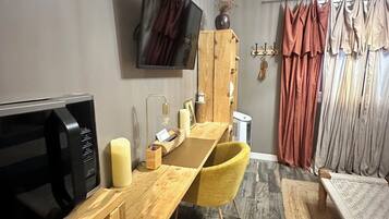 Een knus woongedeelte met een eethoek, een flatscreen televisie aan de muur, een houten kast en een raam met gordijnen.
