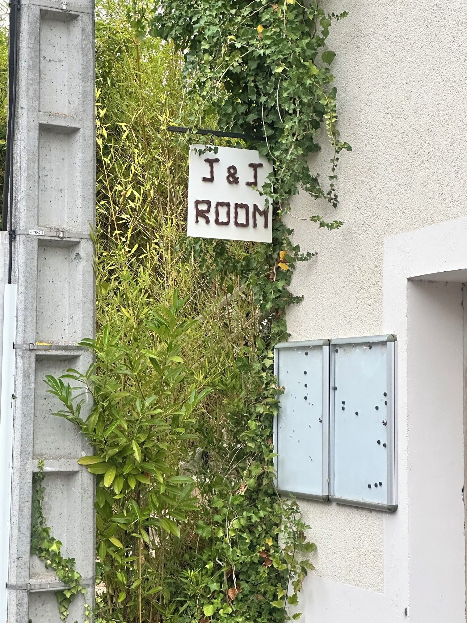 Une enseigne indiquant « J & J ROOM » est fixée à un bâtiment dont la structure est en béton et qui est doté de boîtiers électriques en métal.