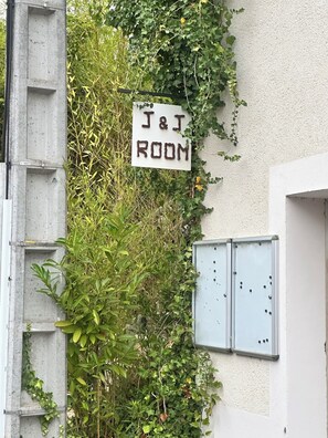 Une enseigne indiquant « J & J ROOM » est fixée à un bâtiment dont la structure est en béton et qui est doté de boîtiers électriques en métal.