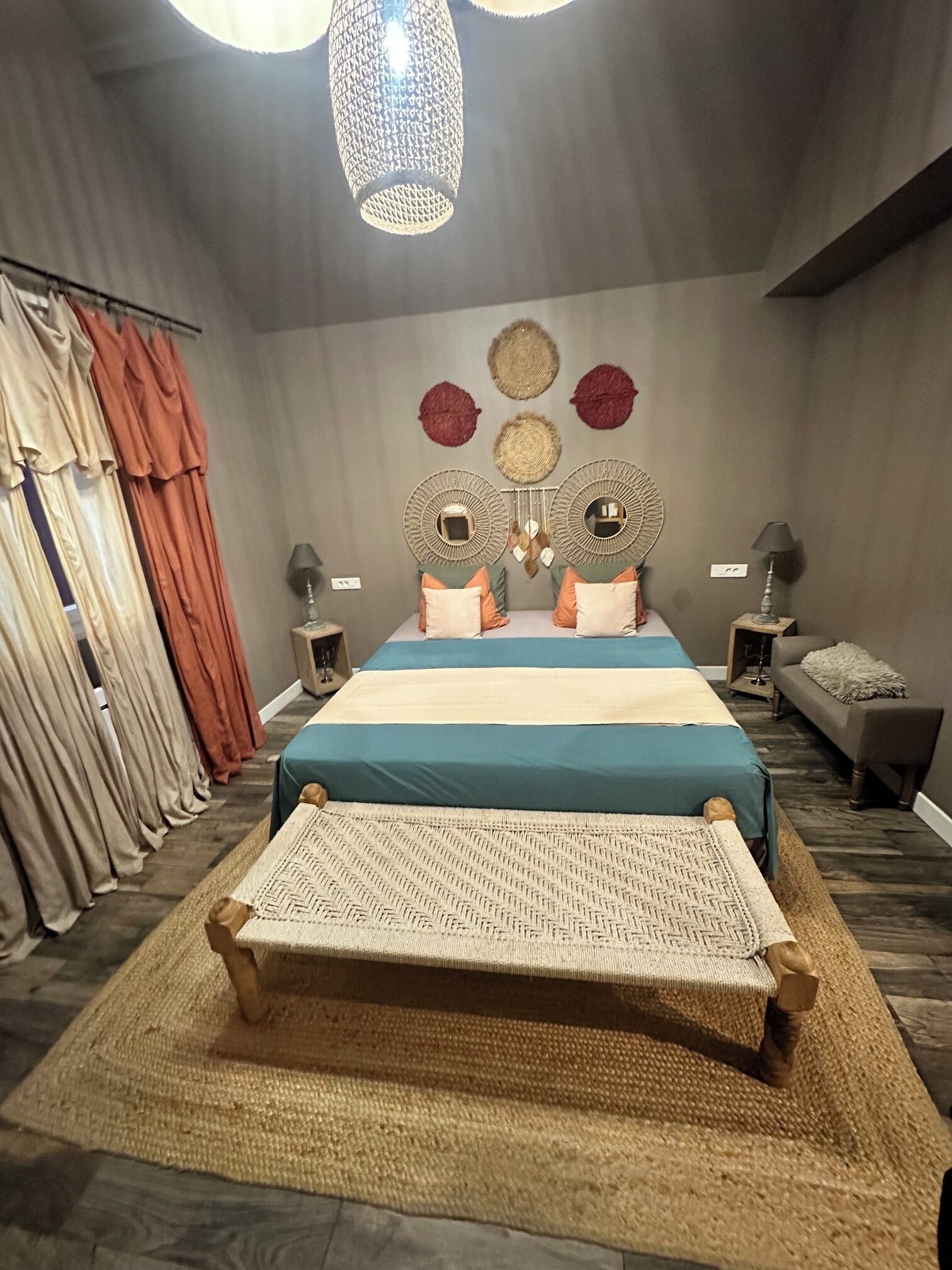 Een slaapkamer met een bed, nachtkastjes, een bankje, gordijnen en decoratie aan de muur.