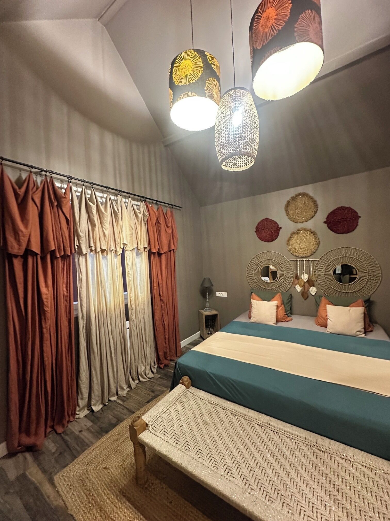 Un dormitorio con cama, cortinas, cabecera con espejos y luces colgantes.