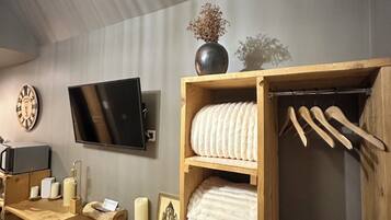 Een kamer met een houten bureau, een aan de muur bevestigde televisie, een houten kledingkast met hangende kleding en een stoel.