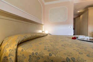 Une chambre d’hôtel avec un lit, une table de chevet, une lampe de chevet et une couvre-lit à motifs floraux.