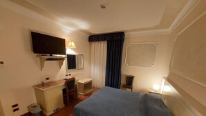 Une chambre d’hôtel équipée d’un lit, d’un bureau, d’une chaise, d’une télévision et d’une fenêtre avec des rideaux.