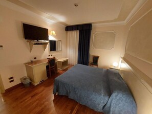 Une chambre d’hôtel équipée d’un lit, d’un bureau, d’une chaise, d’une télévision et d’une fenêtre avec des rideaux.