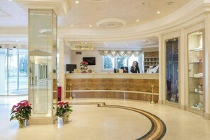 Un hall d’hôtel avec un comptoir en marbre, un bureau d’accueil, un téléviseur et une grande fenêtre donnant sur des arbres.