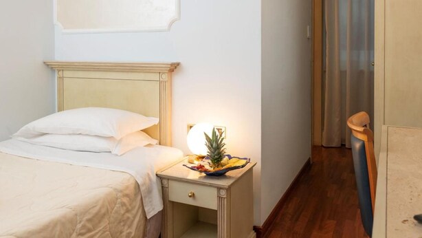 Une chambre d’hôtel avec un lit, une table de chevet avec une lampe, une petite plante et une chaise en bois.