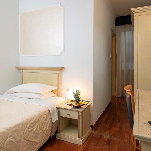 Une chambre d’hôtel avec un lit, une table de chevet avec une lampe, une petite plante et une chaise en bois.