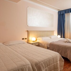 Une chambre d’hôtel avec deux lits, une table de chevet avec une lampe et une grande fenêtre avec des rideaux.
