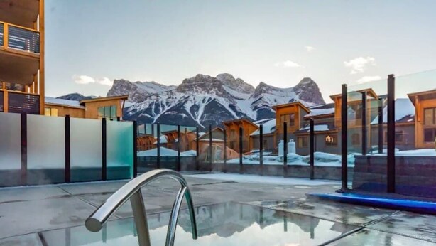 Un hotel moderno con area piscina vetrata, cabine in legno e uno sfondo montuoso.